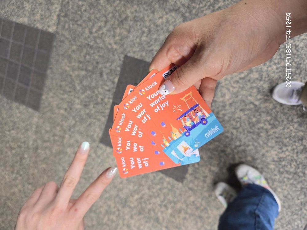 Hands holding orange BTS Rabbit Cards from Klook for Bangkok Skytrain access