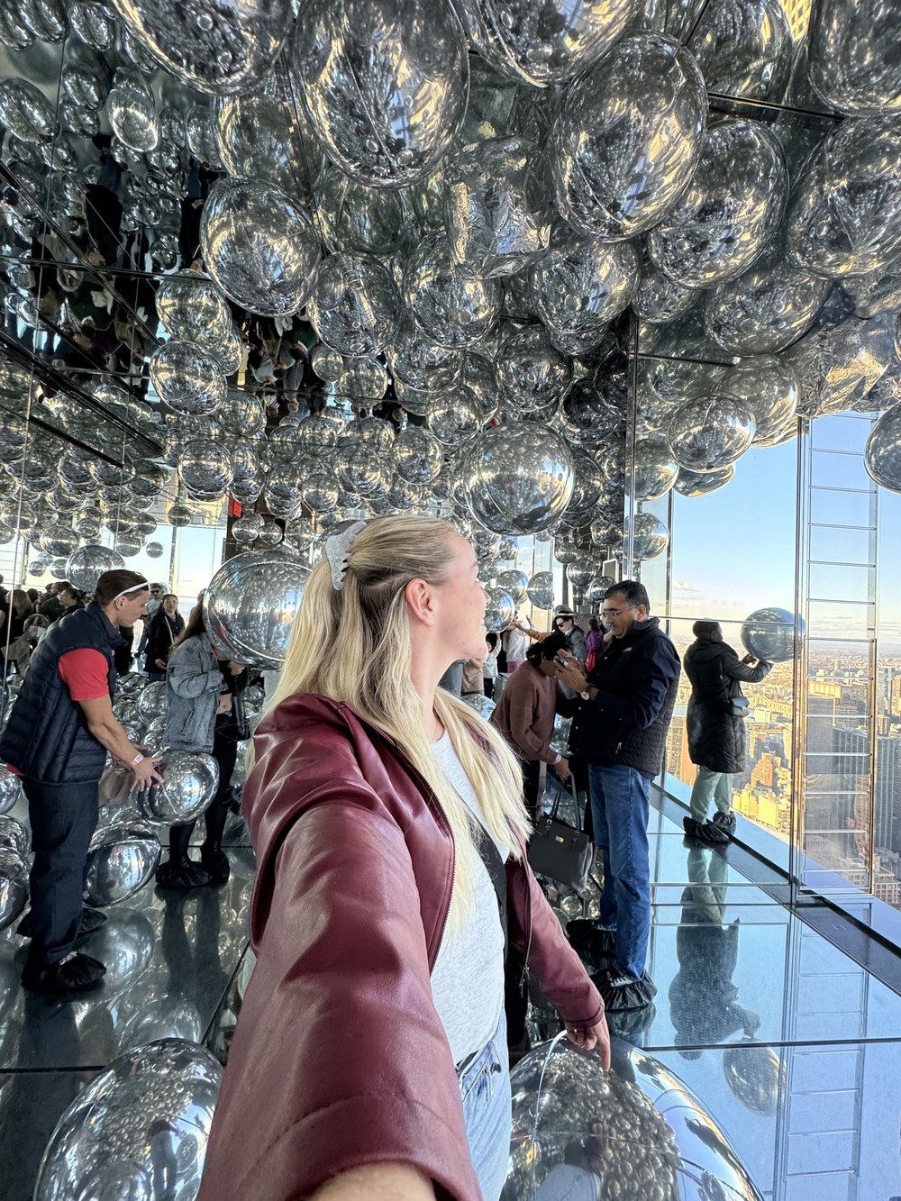 Woman in mirrored observation room filled with reflective silver orbs at Summit One Vanderbilt