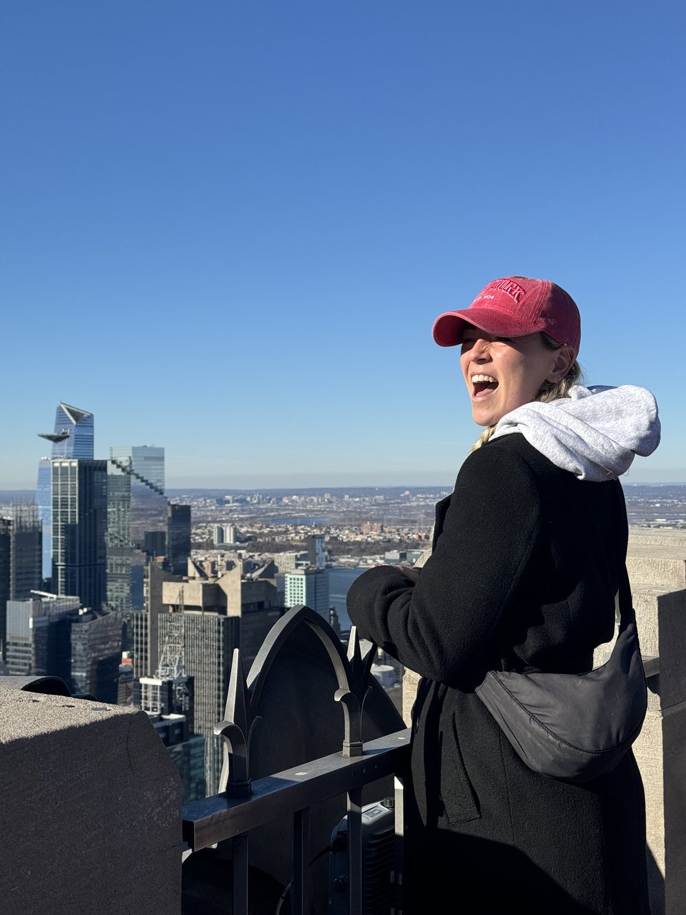 Woman smiling with NYC skyline behind her on Top of the Rock observation deck