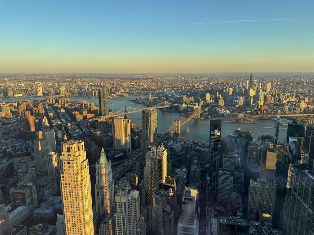 Golden hour view of NYC skyline and East River from One World Observatory's indoor deck