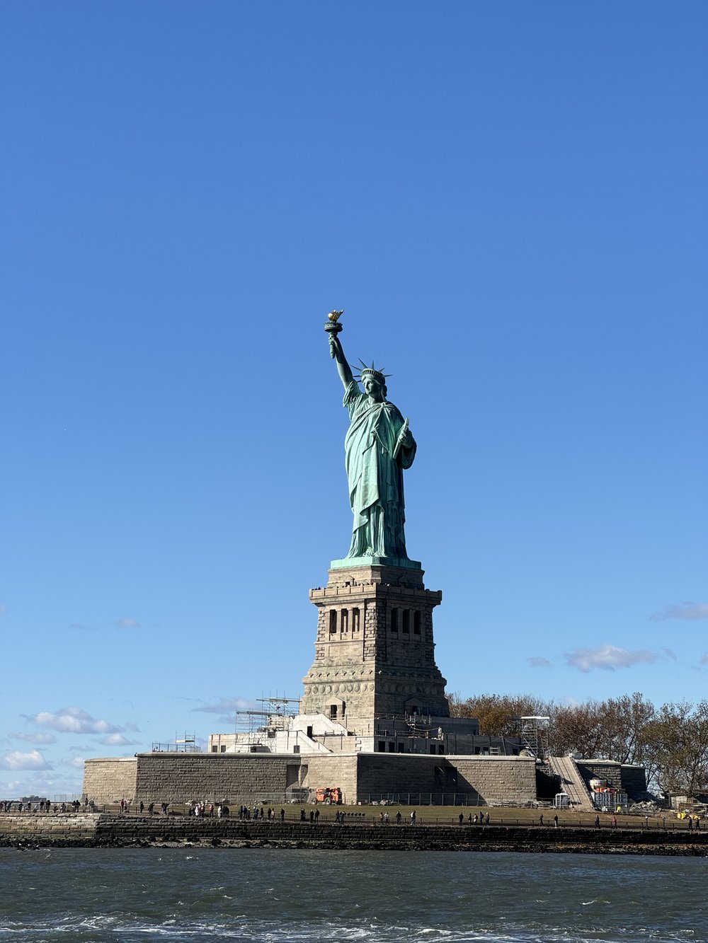 Statue of Liberty standing tall under a clear blue sky, seen from the water.