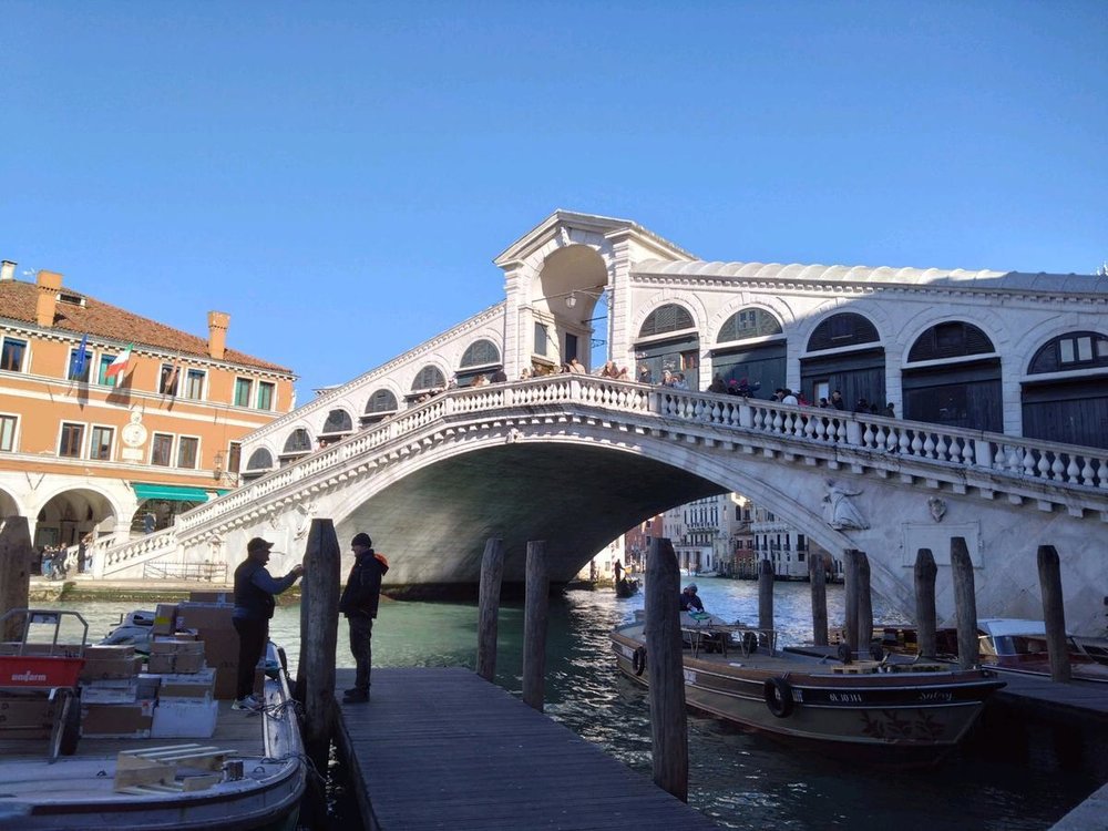 Locals and boats at the base of Rialto Bridge in Venice