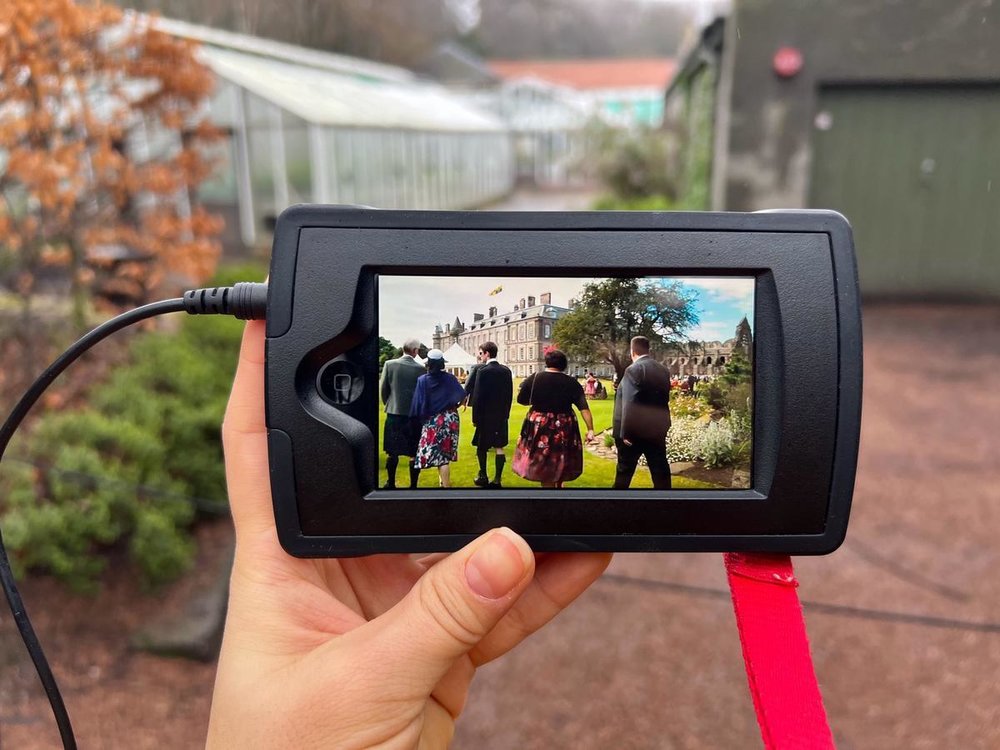 Hand holding a multimedia device showing royal gardens at Holyrood Palace