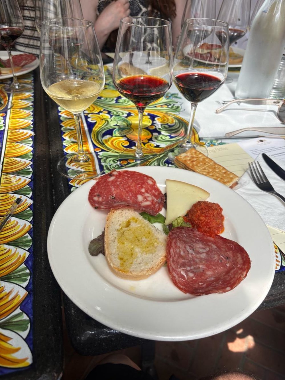 Wine glasses with red and white wines beside a plate of salami, cheese, and bread