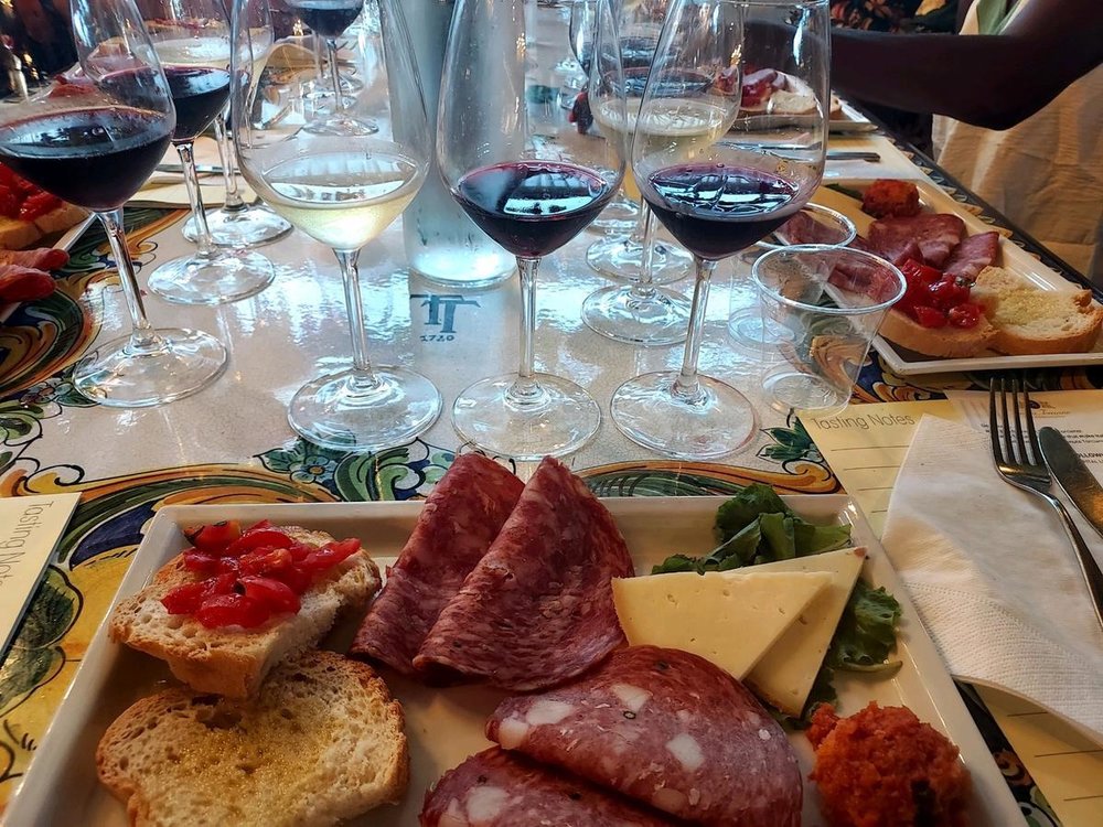 Plate of salami, cheese, and bread beside red and white wine glasses on a tasting table