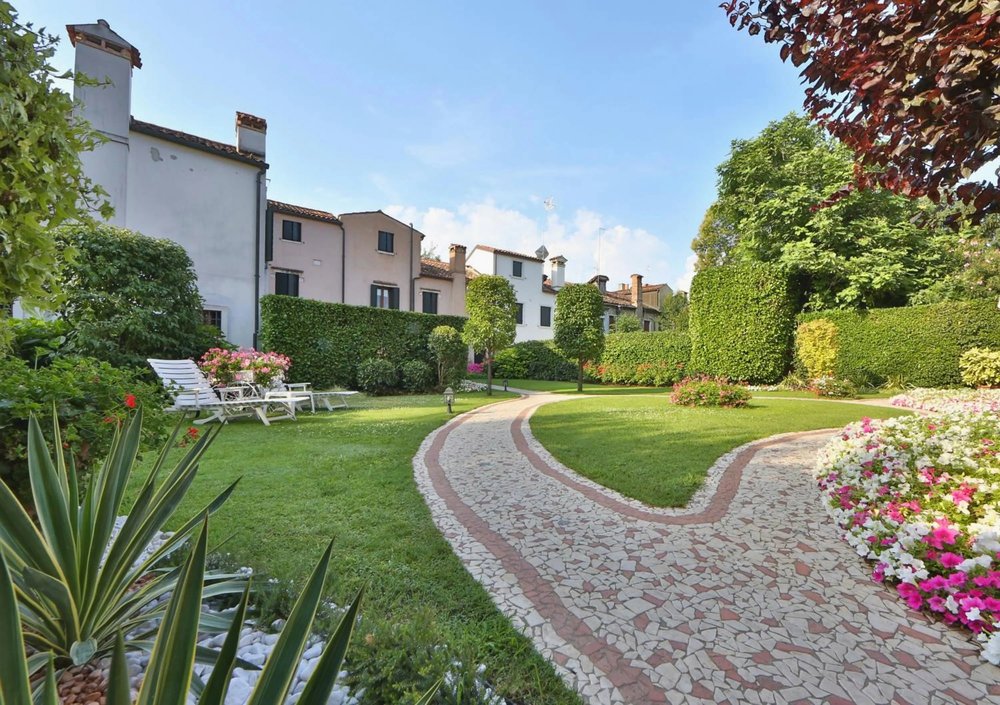 A serene garden path winds through the lush grounds of Hotel Olimpia