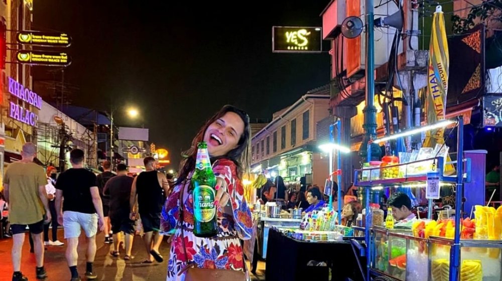 woman smiling and holding a bottle of beer in front of khao san road, bangkok