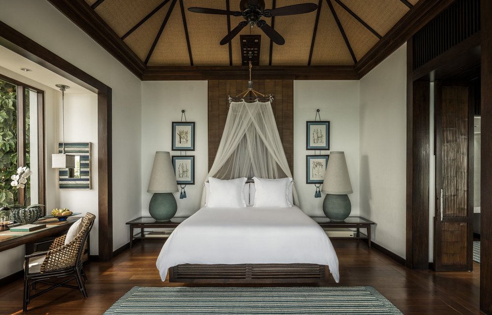 A wide shot of a room inside a villa with a king-sized bed and high ceilings