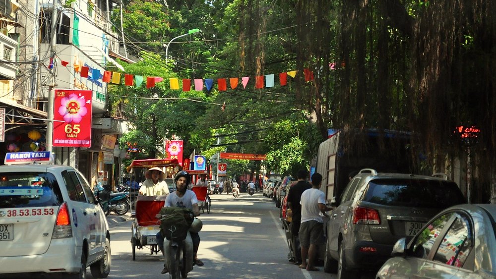 Busy street with taxis, motorbikes, and flags in Hanoi Old Quarter