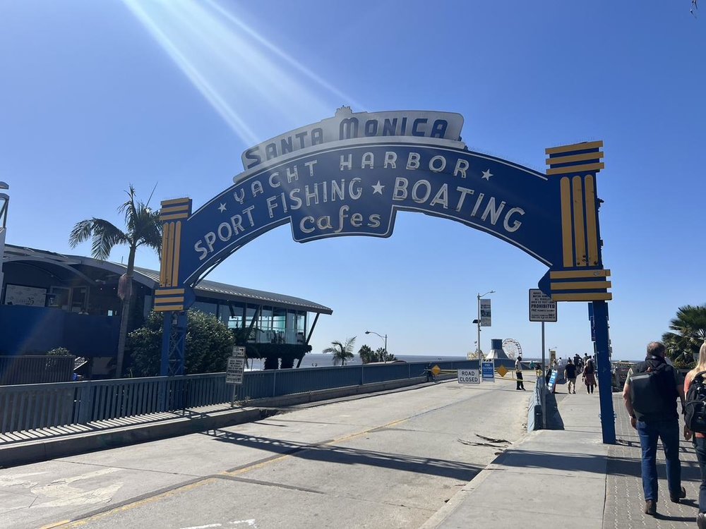 Santa Monica Pier entrance sign with people walking toward the beach.