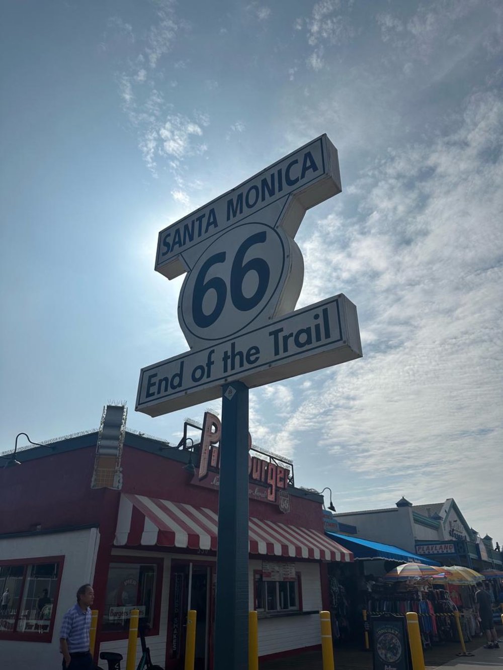 Route 66 End of the Trail sign on Santa Monica Pier under a bright sky.