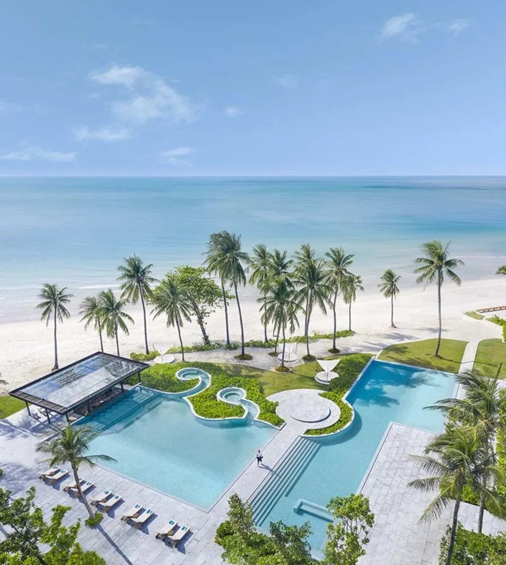 Aerial view of Centara Reserve Samui’s beachfront pool and palm-lined shore.