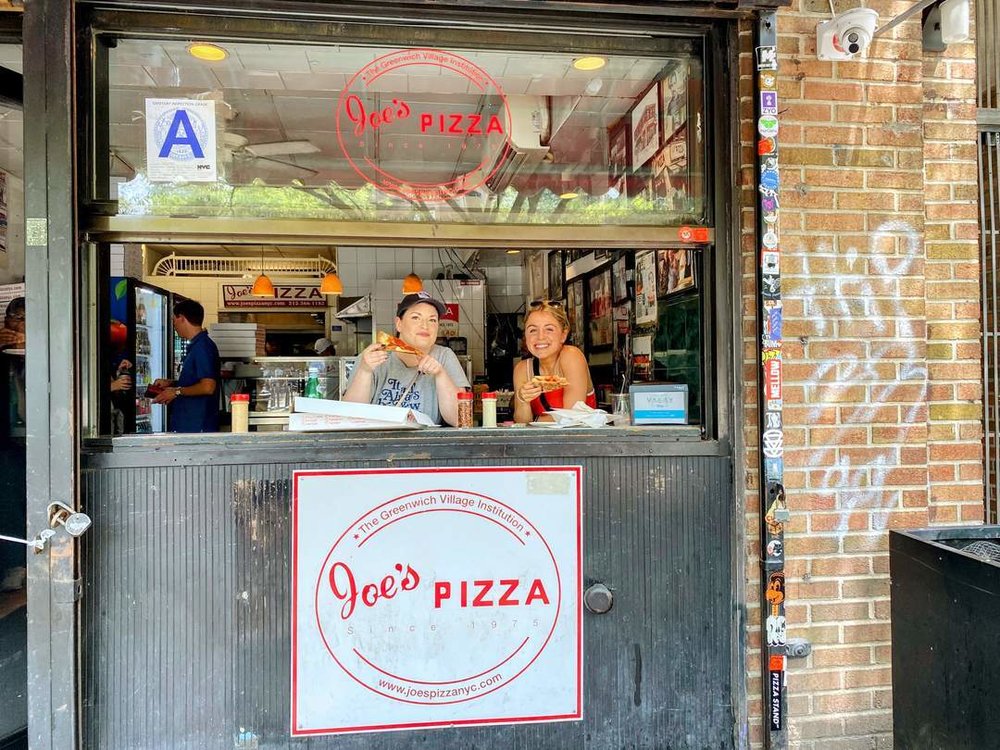 Diners enjoying pizza at Joe’s Pizza window in Greenwich Village, NYC.