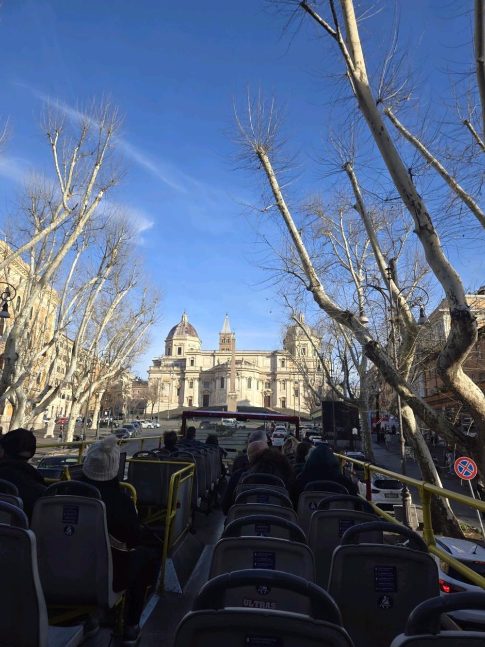 Passengers on a hop-on-hop-off bus in Rome with basilica views and clear skies