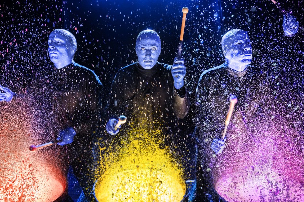 Blue Man Group drumming with vibrant paint during Las Vegas performance.