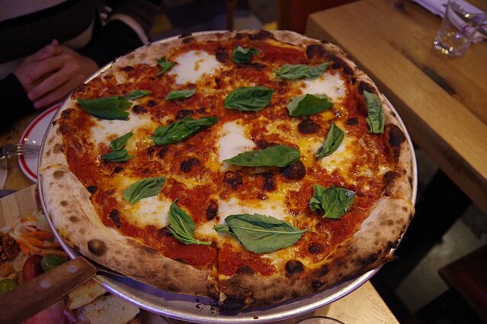 Margherita pizza with basil leaves and melted cheese on a metal tray.