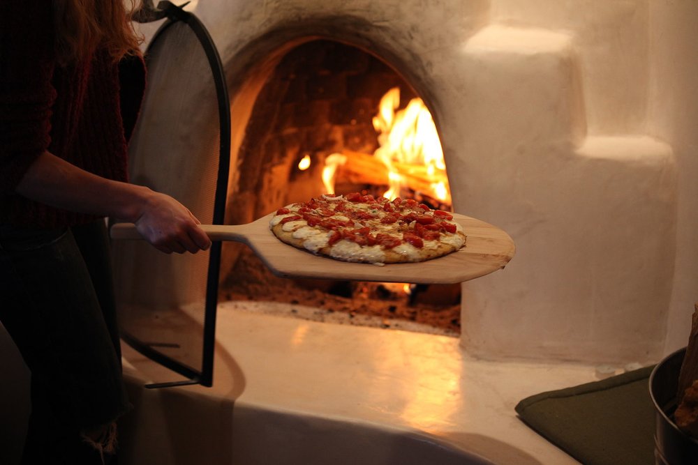 Pizza being placed into a wood-fired oven with flames.