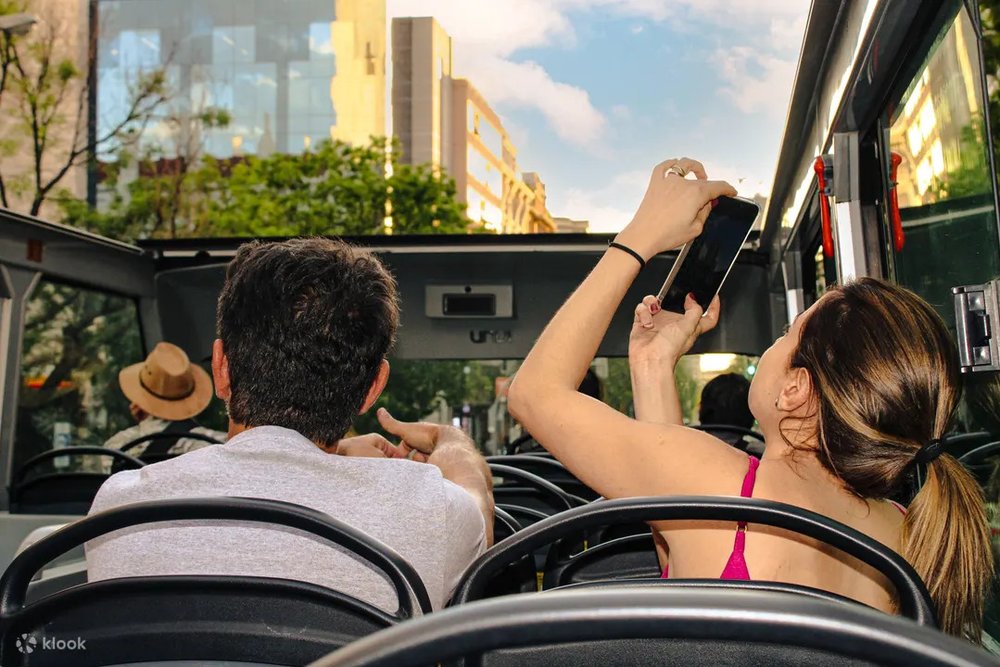 Passengers taking photos from the open-top deck of a Madrid sightseeing bus
