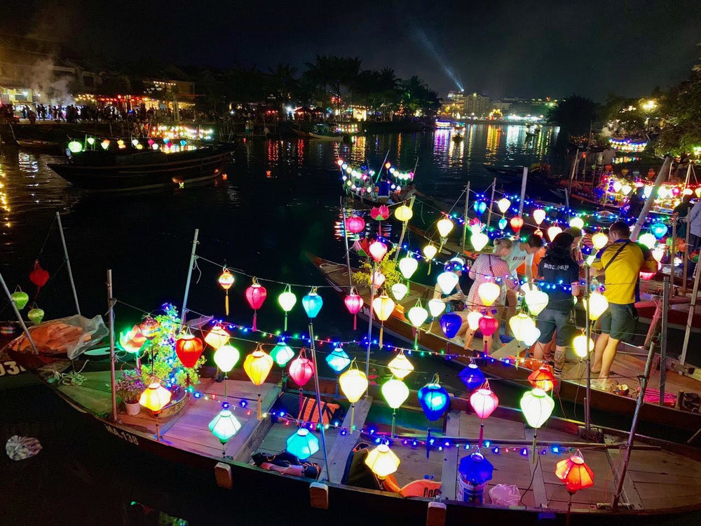 Lantern-covered boats glowing along the Hội An night market at night