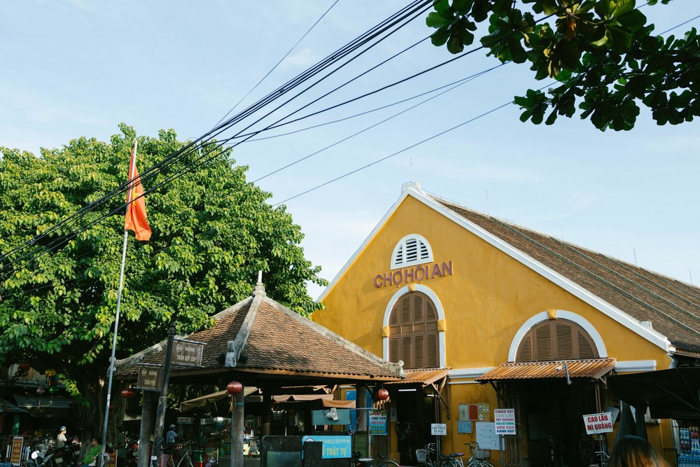 Yellow Hoi An Central Market building surrounded by vendors and tree