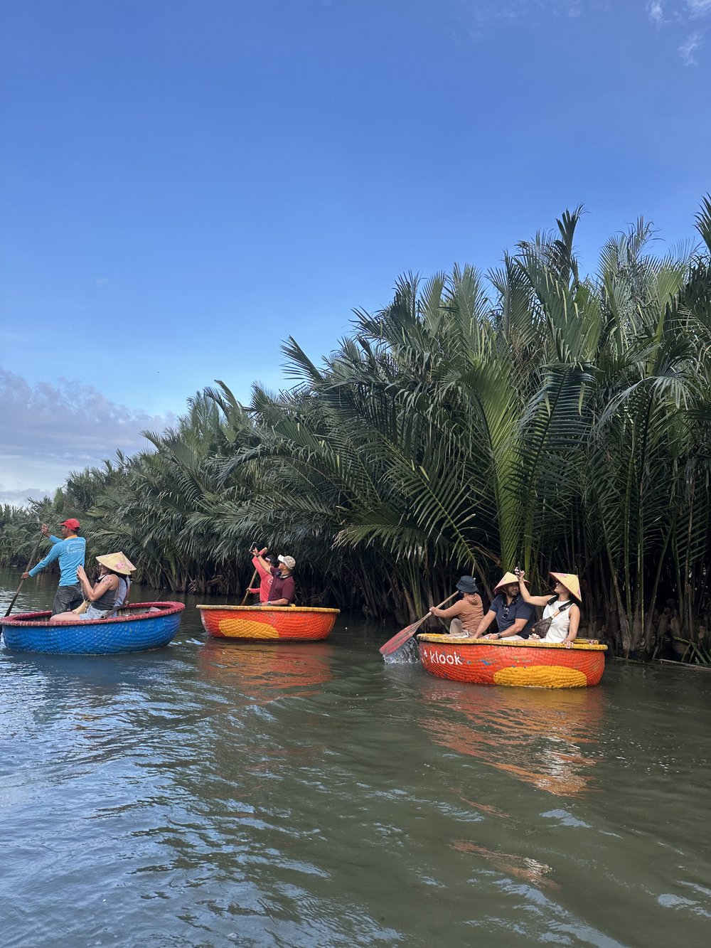 Tourists paddling bright coconut boats along a palm-lined river
