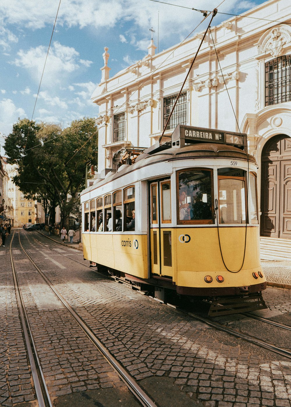 Lisbon tram traveling uphill past old architecture and trees