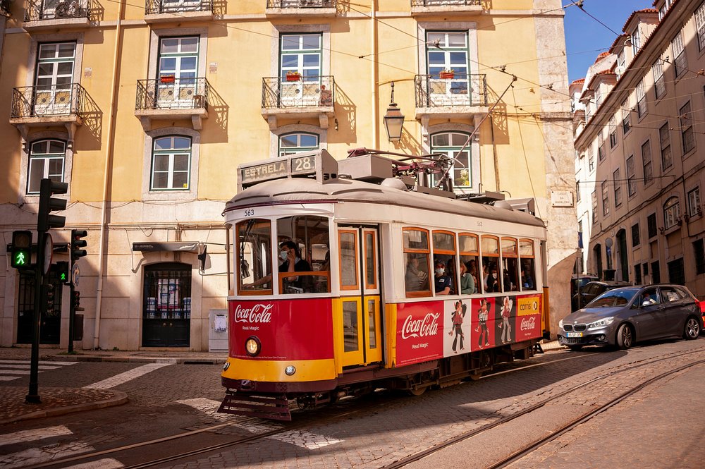 Red-and-yellow Tram 28 traveling past historic Lisbon buildings on a bright day