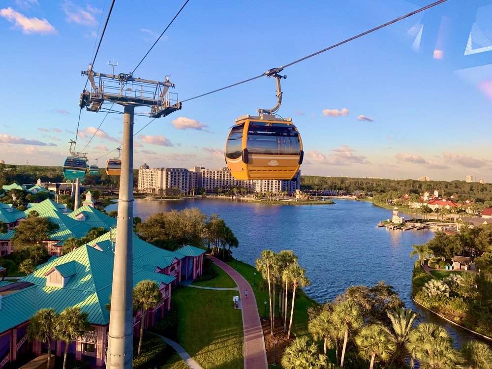 Aerial view of Disney Skyliner gondolas above resort rooftops and water
