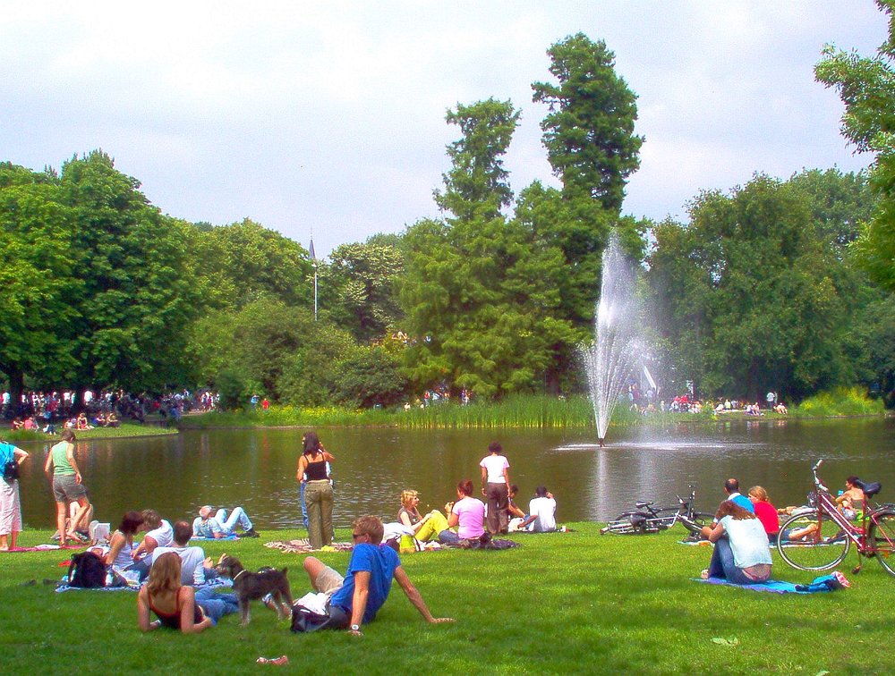 Visitors lounging on the grass near a pond and fountain at Vondelpark, Amsterdam