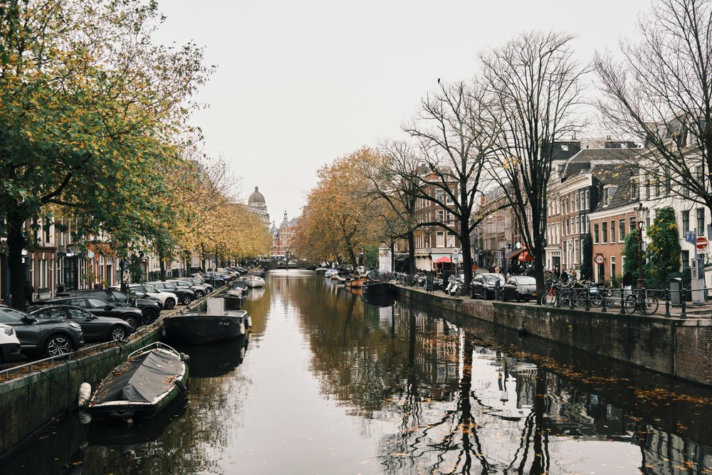 Amsterdam canal lined with fall trees, boats, and classic Dutch buildings