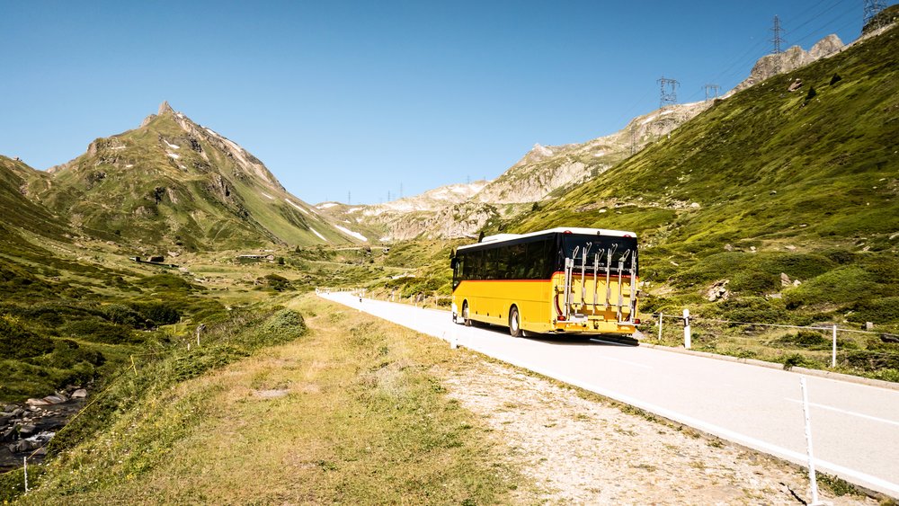 Yellow Swiss PostBus traveling along a scenic Alpine mountain road