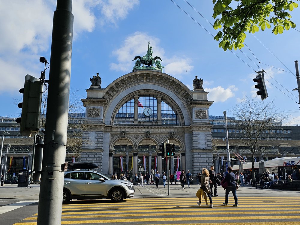 Historic Lucerne station building with crowds and car in front