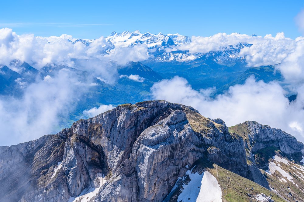Aerial view of Mount Pilatus cliffs with snowy Alps and clouds in the background