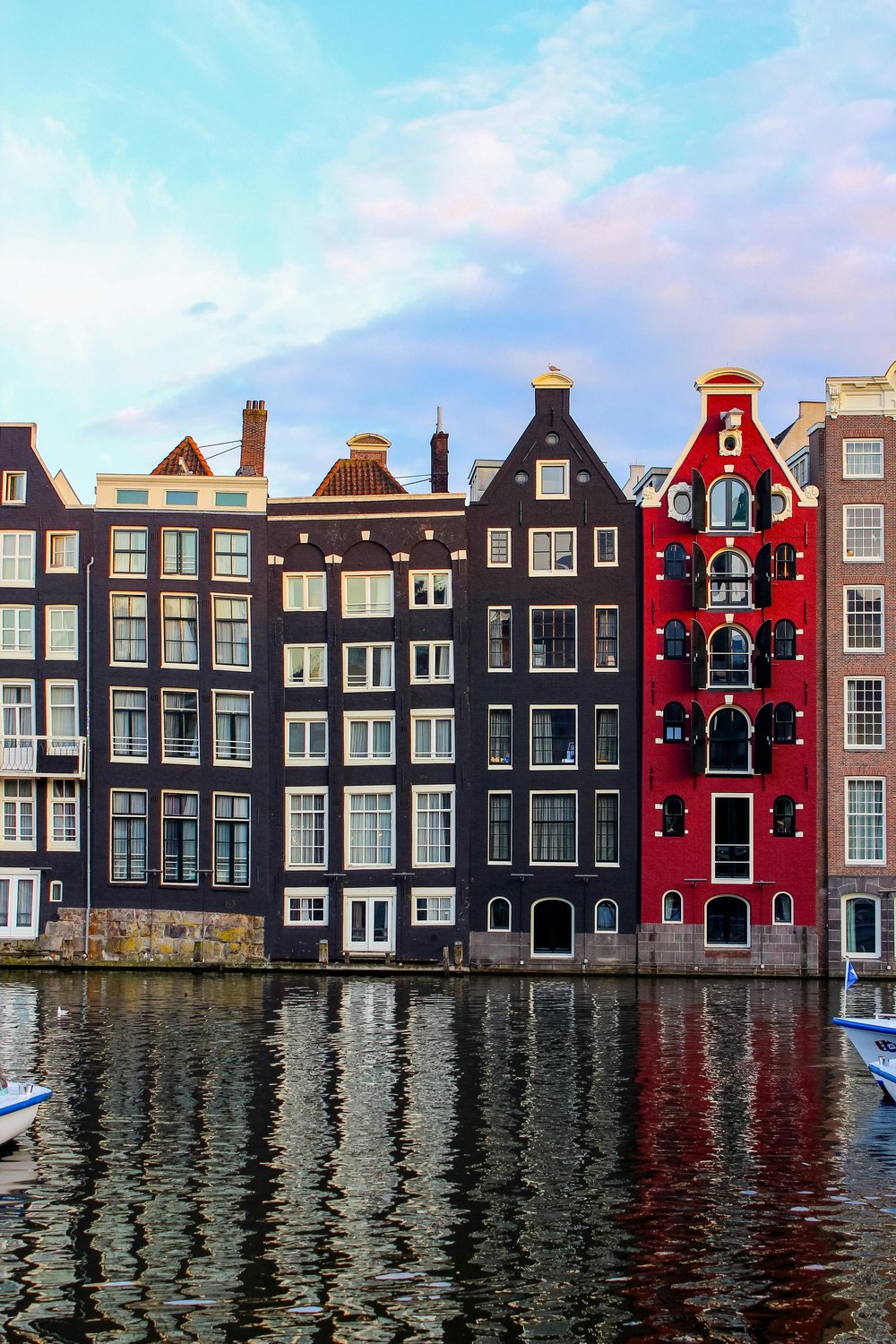 Row of tall, narrow canal houses reflecting on the water in Amsterdam
