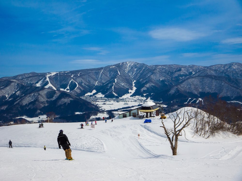 นักท่องเที่ยวเล่นสกีบนลานหิมะในญี่ปุ่นพร้อมภูเขาหิมะเป็นฉากหลัง