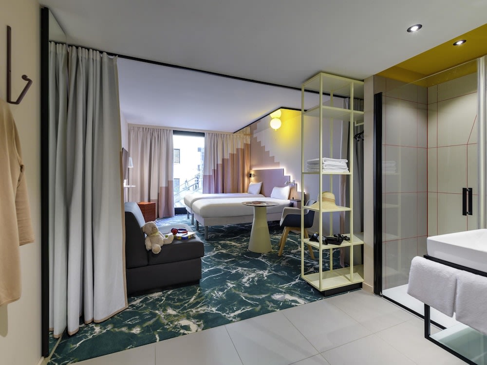 A picture of the hotel room, showing the bathroom, the bed, a window next to the bed, and a chair at the foot of it