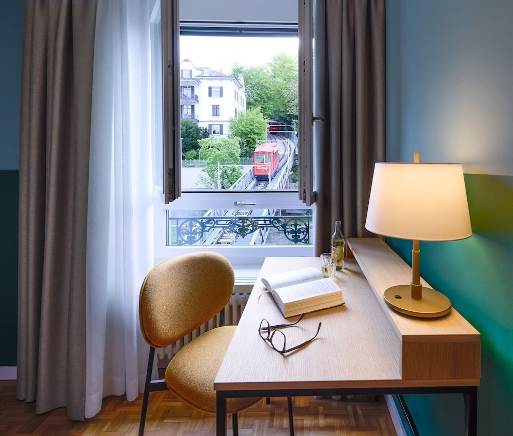 A study desk pushed to the side where a window overlooks a passing funicular
