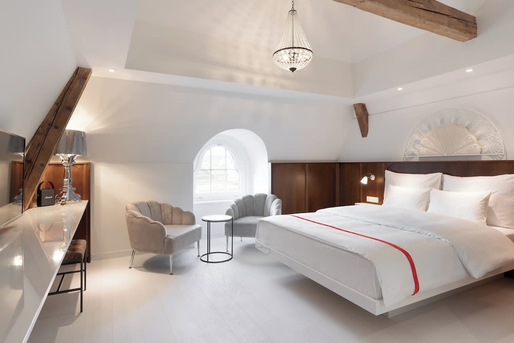 A white room with wooden beams, a white bed, and a window
