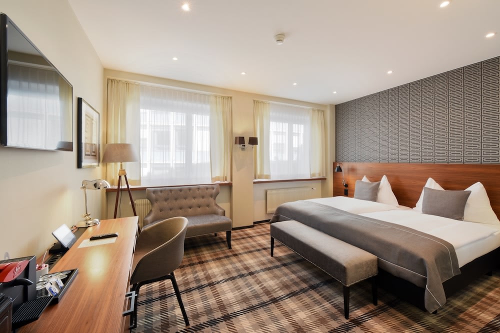 A photo of the hotel room, with its bed, small sofa, study desk, TV, and windows