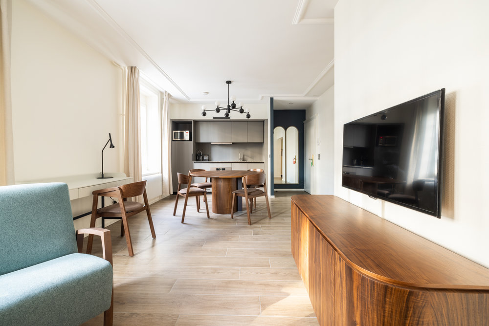 The hotel room’s spacious living area, with a sofa, a TV, a study desk, a dining area, and a kitchenette