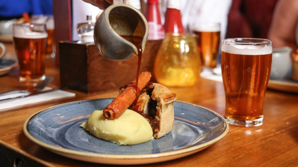 Classic British pub food with meat pie, mash, gravy, and beer on a wooden table.