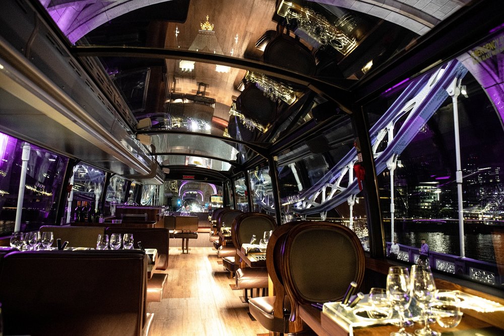 Interior of Bustronome luxury dining bus with tables, glass roof, and London city views