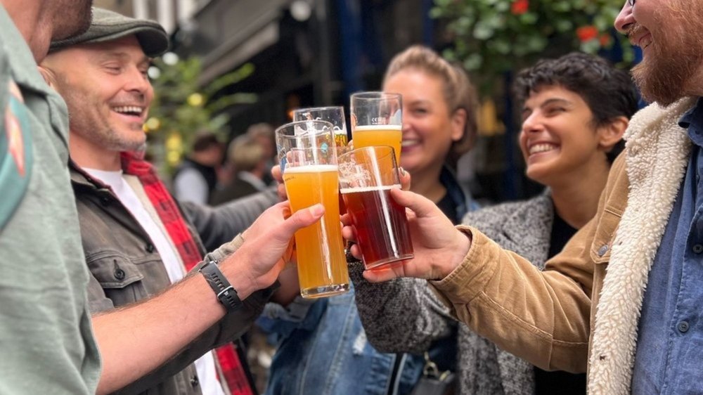 Group of friends clinking beer glasses at a London pub outdoor setting
