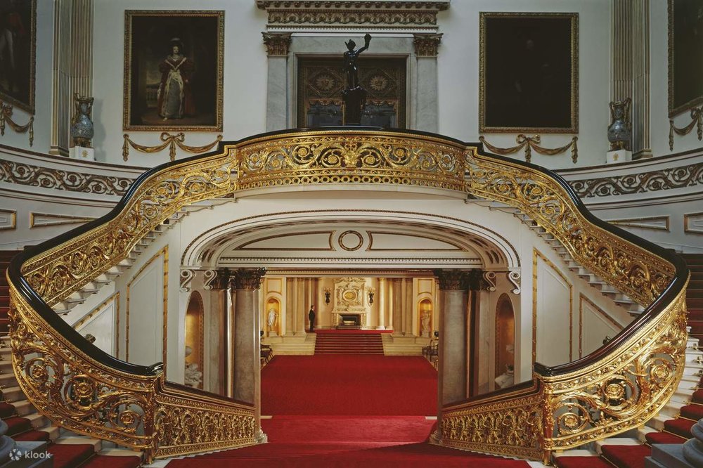 Ornate gold staircase and red carpet inside Buckingham Palace