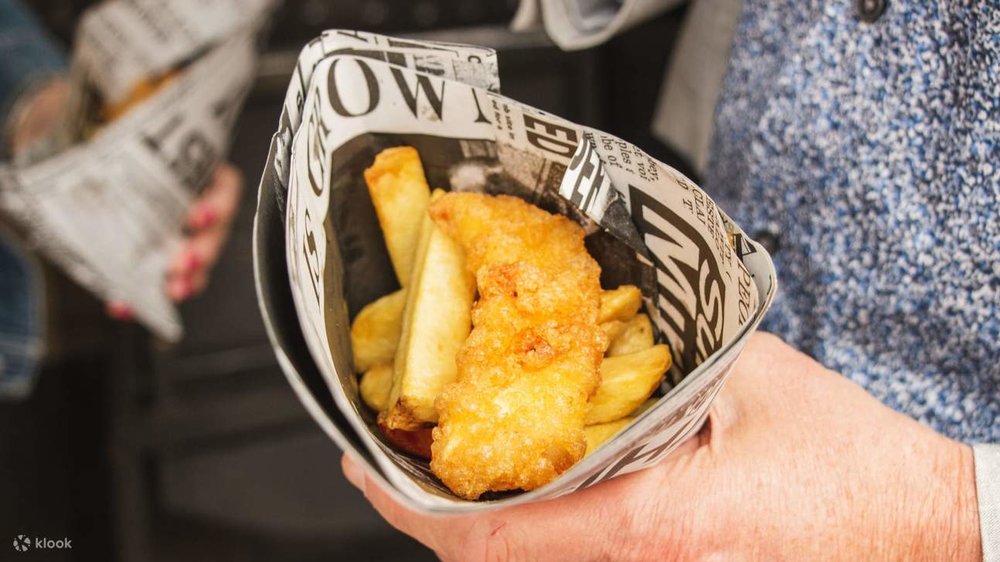 Hand holding a paper cone of fish and chips at a London food market