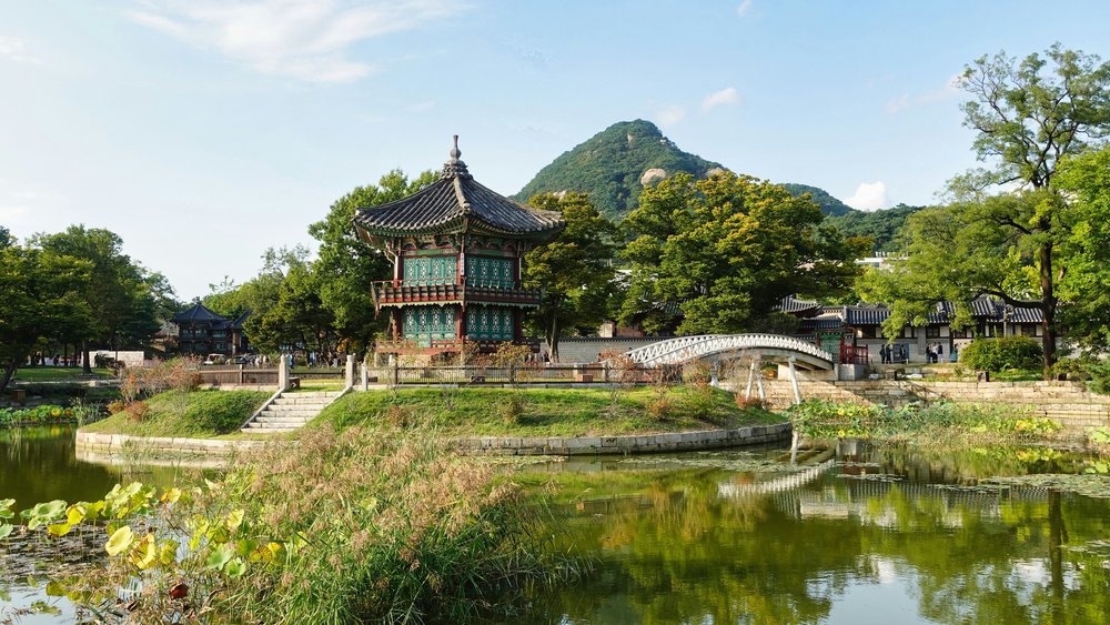 Traditional Korean palace and pavilion with green trees and mountain backdrop in summer