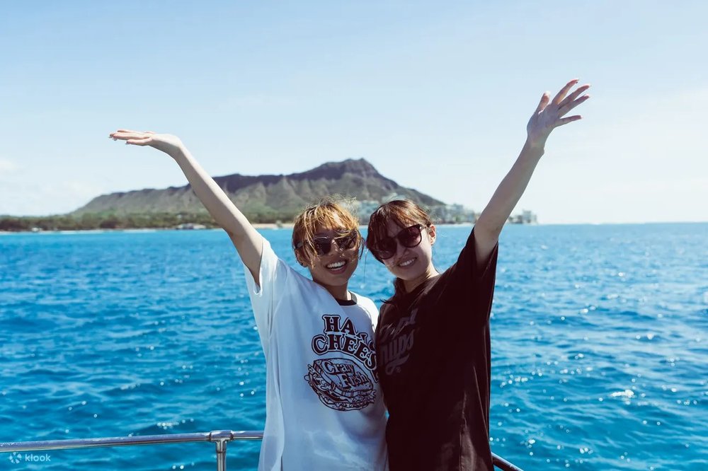 Two women posing for a picture with the Waikiki beach as their background, at a sunset cruise.