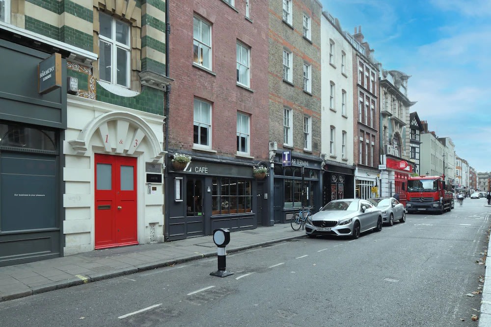 Soho London street with historic buildings, cafés, and parked cars