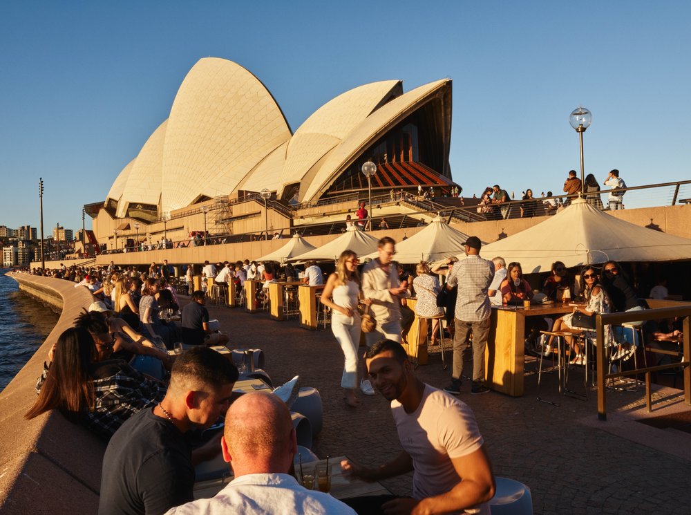 People enjoying drinks and views outside the Sydney Opera House at sunset