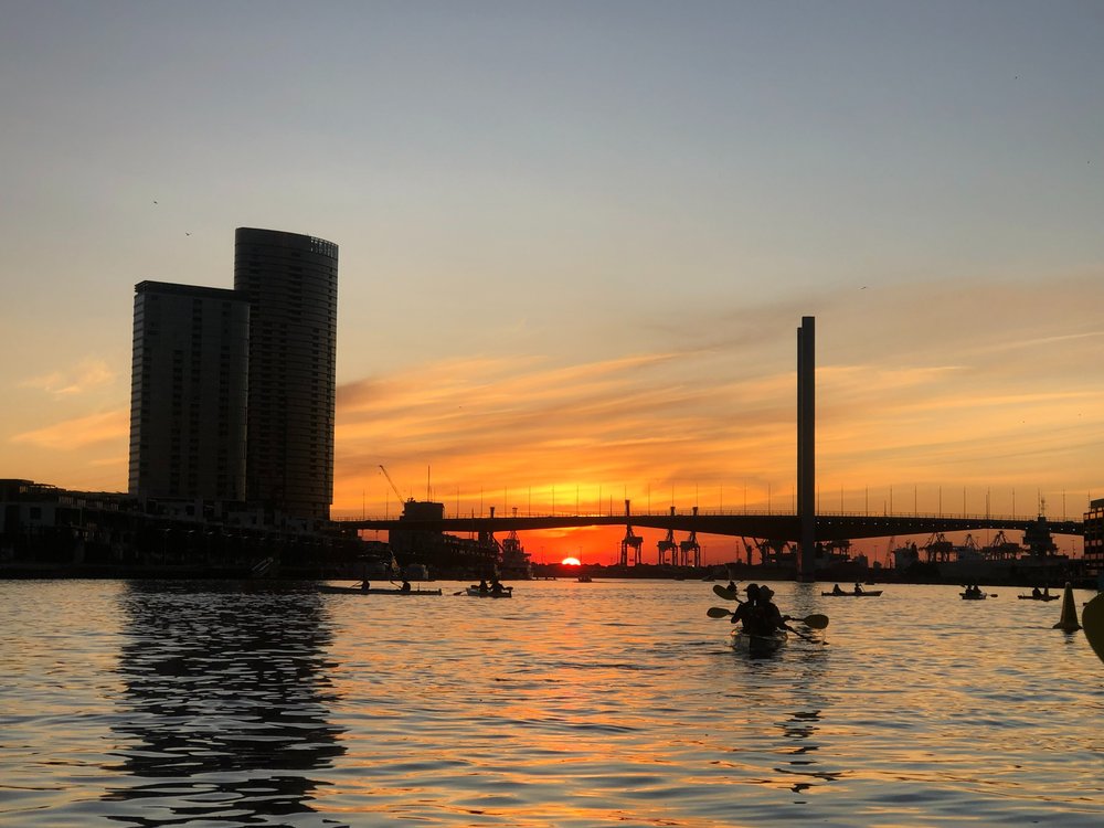 Kayakers paddling on the Yarra River at sunset with Melbourne city skyline in the background